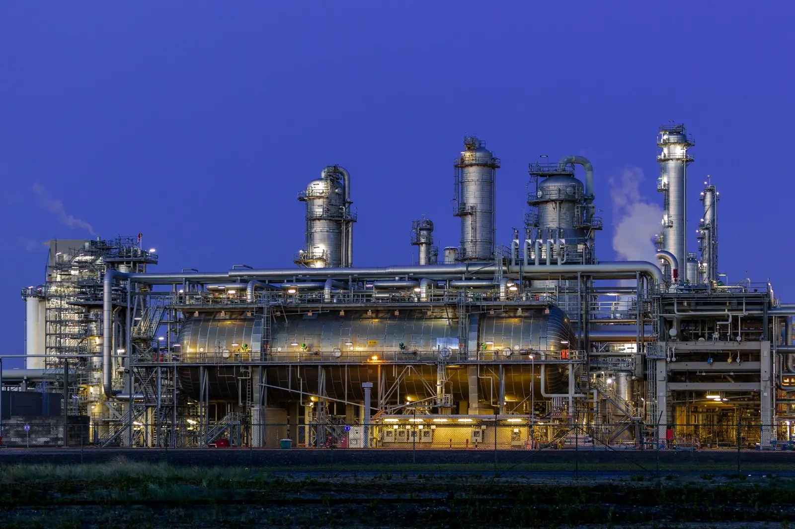 Refinery lit up at dusk, with towers and tanks