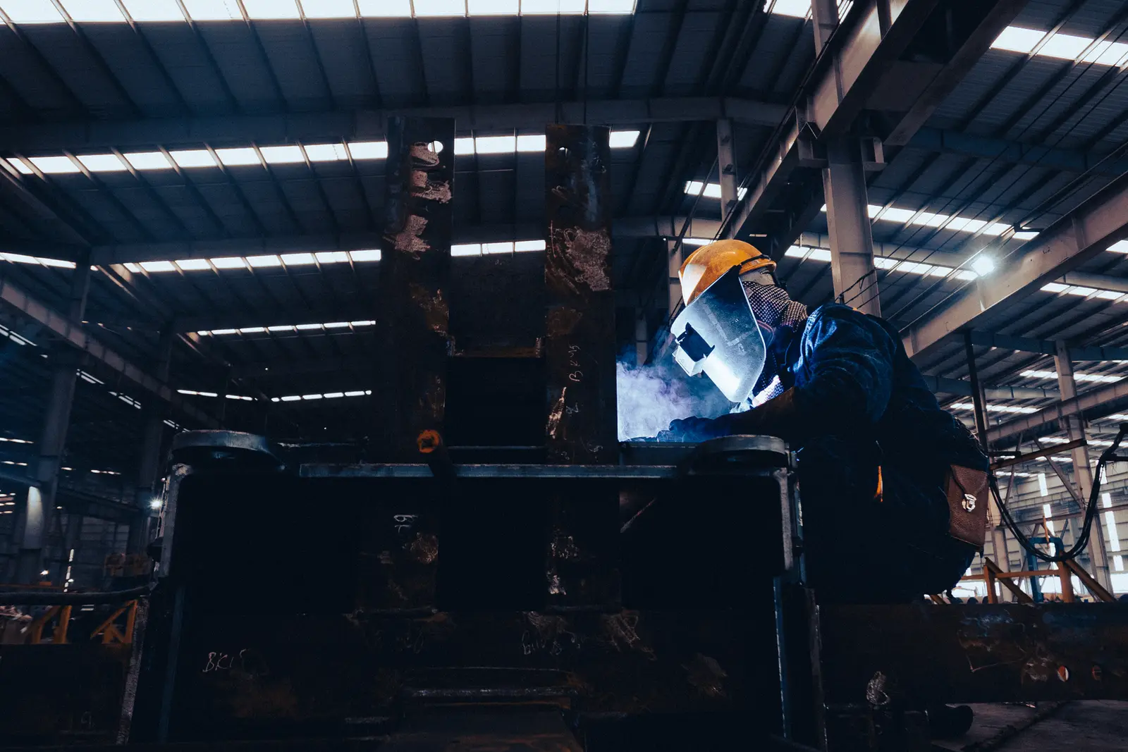 Welder in a mask works in a dark industrial shop as sparks fly